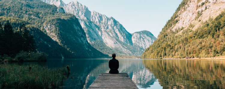 A man sitting and meditating in front of a quiet lake to reduce chronic stress and lose weight